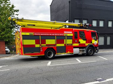 Manchester, İngiltere - 25 Eylül 2025: Manchester 'da bir şehir yolunda, harekete hazır merdiveni olan parlak bir itfaiye aracı.