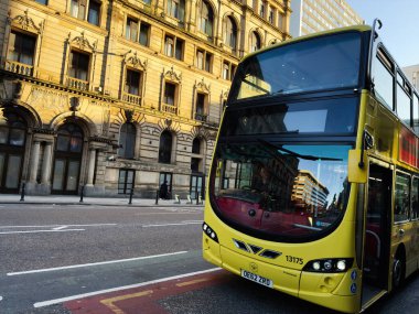 Manchester, İngiltere - 25 Eylül 2025: Manchester City caddesinde tarihi mimari ve pencerelerdeki yansımaların yanında parlak sarı otobüs.