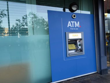 Manchester, İngiltere - 25 Eylül 2025: Cam ambarın yanındaki binanın üzerine monte edilmiş mavi ATM birimi; kentsel bankacılık ve güvenlik özellikleri.