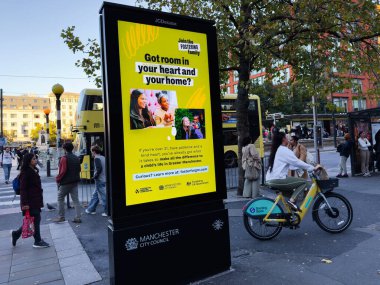 Manchester, İngiltere - 25 Eylül 2025: Kamuya açık şehir manzarası, sarı renkli bir koruyucu reklam, insanlar yürüyor, ve Manchester şehrinde bir bisikletçi.