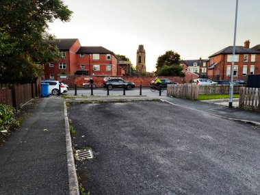 Manchester, İngiltere - 25 Eylül 2025: Park halindeki arabaların, bisikletçilerin, kırmızı tuğlalı evlerin ve uzak kilise kulesinin bulunduğu huzurlu bir yerleşim yeri.