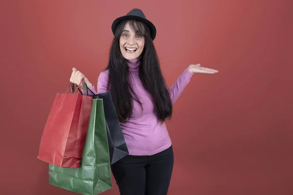 The friendly woman with paper shopping bags, pink sweater, and black hat isolated from the background.