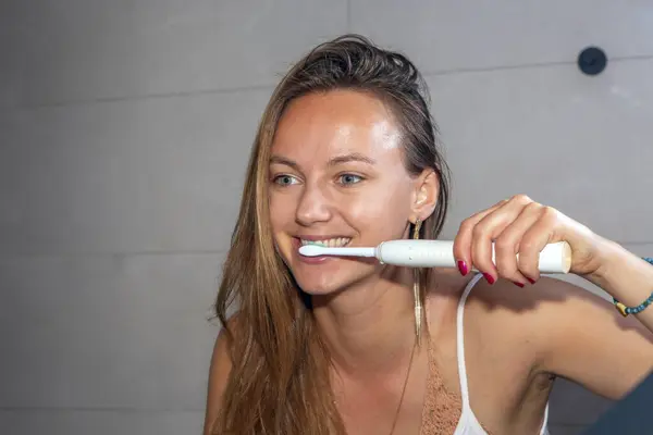 Dişlerini elektrikli diş fırçasıyla fırçalayan hoş bir kadın.