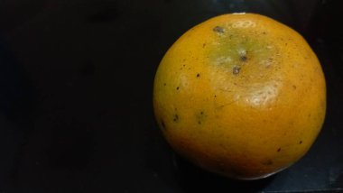 Siyah bir masanın sağında çilli bir portakal.