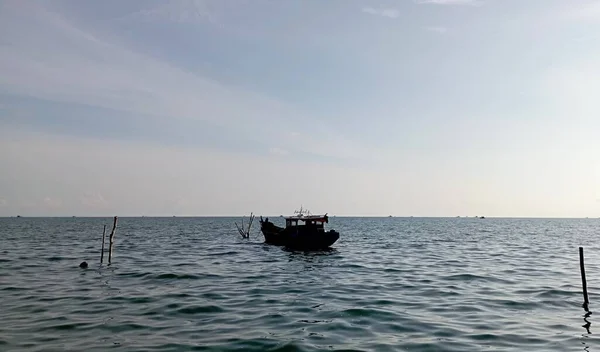 Mavi denizin ortasında bir gemi ya da tekne ve bulutlu beyaz bir gökyüzü.