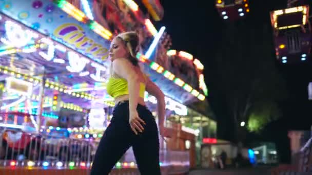 漂亮的金发姑娘晚上在游乐园里跳舞 后面是摩天轮 高质量的4K镜头 — 图库视频影像