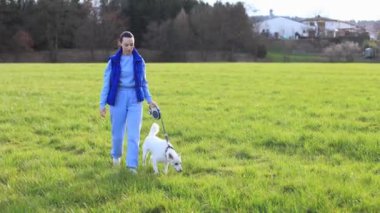 Mavi takım elbiseli bir kız yeşil çimlerde güzel beyaz bir köpekle yürüyor. Yüksek kalite 4k görüntü