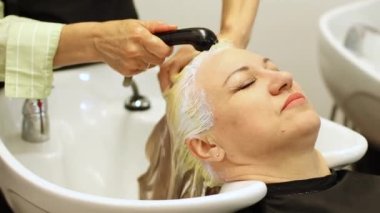 Güzellik salonunda yaşlanmış sarışın bir kadının kafasını yıkamak. Bir kuaförün elleri. Yüksek kalite 4k görüntü