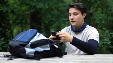 Sırt çantalı erkek turist yaz ormanlarında akıllı telefon manzarasıyla fotoğraf çekiyor. Gezgin blogcu video çeker, fotoğraf çeker. Yüksek kalite 4k görüntü