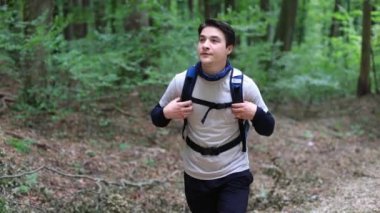 Asyalı adam ormanda yürüyor ve sırt çantasına sarılıp ormanda yürüyüşe çıkıyor. Yüksek kalite 4k görüntü