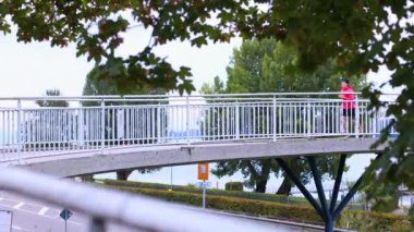 Parlak pembe ceketli genç adam sonbaharda köprü boyunca koşar. Yüksek kalite 4k video yavaş çekim 4k