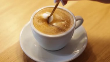 Kremalı bir kahvenin küçük beyaz bir fincanda karıştırıldığı yakın çekim. Yüksek kalite 4k görüntü
