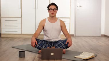 Evde dizüstü bilgisayarla yoga yapan genç bir adam. Karemat 'ta tembel yoga dersleri. Yüksek kalite 4k görüntü