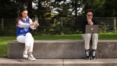 Bilgisayarlı bir adam ve telefonu olan bir kız sokakta karşılıklı oturuyorlar. Yüksek kalite 4k görüntü