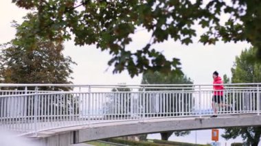 Renkli elbiseli bir koşucu sabahın erken saatlerinde köprüden koşarak geçiyor ve çerçevesi tükeniyor. Yüksek kalite 4k görüntü