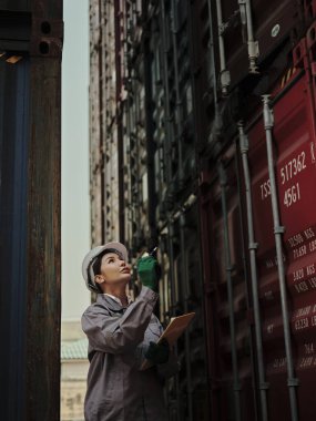 Portrait of a female worker holding clipboard while standing outside a warehouse container . clipart