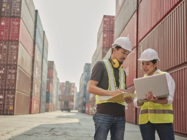 Genç Asyalı kadın ve erkek mühendis deniz aşırı nakliye konteynerinde iş arkadaşlarıyla birlikte çalışıyorlar..