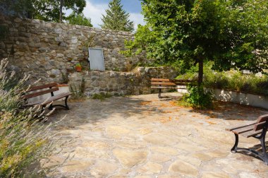 Huzurlu köy meydanında insanların dinlenmesi için ahşap banklar, bir taş kaldırım ve kaya yüzlü istinat duvarı, Annot kırsal dağ komünü, Provencal Alps, Güneydoğu Fransa