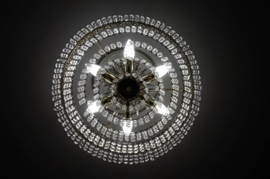 Lüks bir kristal avize, bir oturma odasının tavanında asılı, ve elektrik lambaları aracılığıyla sarı ışık yayıyor, alacakaranlık, karanlık bir ortamda