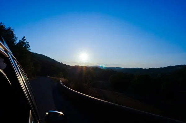 法国南部Aveyron的Massif中央山脉的地平线上升起了耀眼的落日 一条弯弯曲曲的道路穿过田野和森林 模糊了美丽的乡村风景 — 图库照片