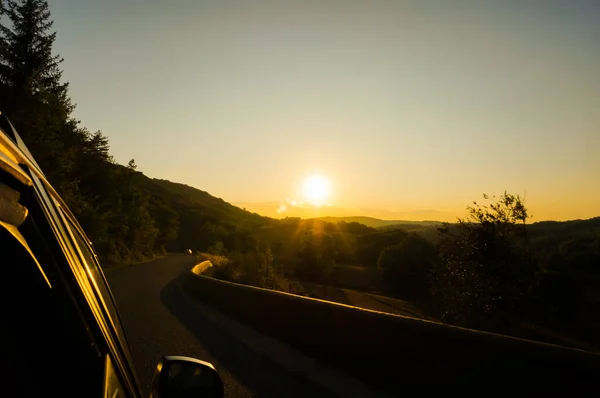 法国南部Aveyron的Massif中央山脉的地平线上升起了耀眼的落日 一条弯弯曲曲的道路穿过田野和森林 模糊了美丽的乡村风景 — 图库照片