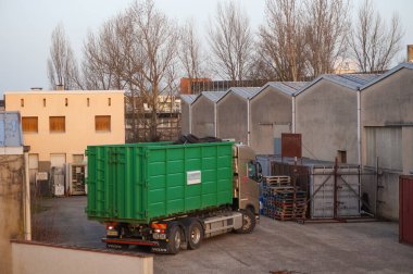 Occitanie, Fransa - Şubat 2021 Fransız geri dönüşüm şirketi Aliapur 'dan bir Volvo kamyonu kullanılmış lastik lastiklerle dolu yeşil bir kovayı bir deponun avlusuna yüklüyor.