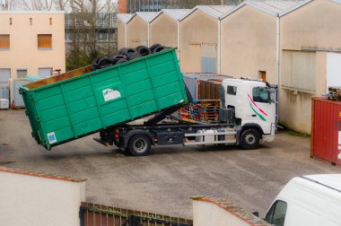 Occitanie, Fransa - Şubat 2021 Fransız geri dönüşüm şirketi Aliapur 'dan bir Volvo kamyonu kullanılmış lastik lastiklerle dolu yeşil bir kovayı bir deponun avlusuna yüklüyor.