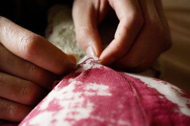 Dişi bir modacının eline yakın çekim. Dikiş atmada ustaca kullanılıyor. Ve eski, hasarlı oyuncak bir hayvanın kırmızı renkli kumaşını onarıyor.