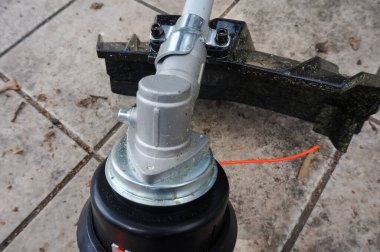 Alman yapımı bir benzin fırçası maketinin çelik ve plastik makine parçaları: döner kafaya sabitlenmiş naylon makara ve sürücü gövdesinin sonunda kesilmiş çimen kalıntıları ile güvenlik.