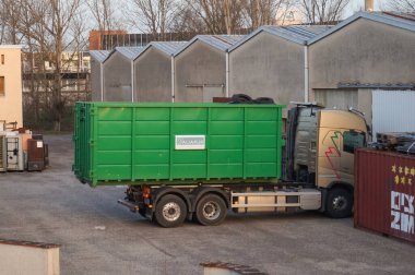 Occitanie, Fransa - Şubat 2021 Fransız geri dönüşüm şirketi Aliapur 'dan bir Volvo kamyonu kullanılmış lastik lastiklerle dolu yeşil bir kovayı bir deponun avlusuna yüklüyor.