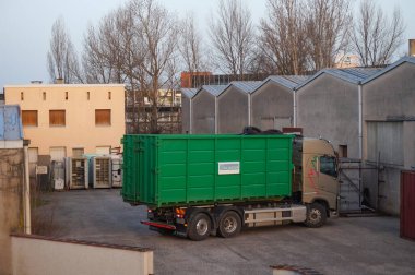 Occitanie, Fransa - Şubat 2021 Fransız geri dönüşüm şirketi Aliapur 'dan bir Volvo kamyonu kullanılmış lastik lastiklerle dolu yeşil bir kovayı bir deponun avlusuna yüklüyor.