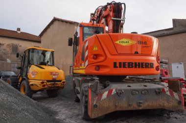 Tarn, Fransa - Şubat 2021 - Bir şantiyede iki tekerlekli inşaat makinesi: Colas tarafından işletilen turuncu bir Liebherr kazıcısı ve Loxam tarafından kiralanan sarı eklemli bir yükleyici