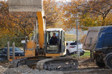 Reims, Fransa - Kasım 2022 - Bir işçi, Alman-İsviçreli üretici Liebherr 'den sarı bir mekanik kazıcıyı çalıştırıyor, yanındaki çöp kamyonu kazıyı boşaltmaya hazır.