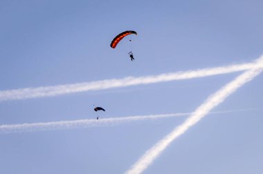 İki paraşütçü açık mavi gökyüzünde paraşüt dalışı yapıyor. Jet kontrastı, Fransa 'nın Albi-Le Sequestre Havaalanı' na inmeye hazırlanıyor.