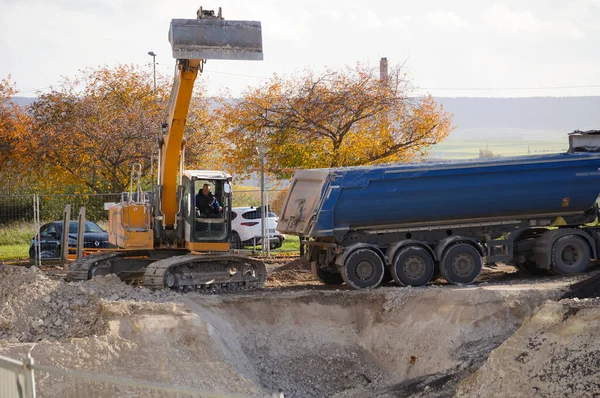 stock image Reims, France - Nov. 2022 - A yellow excavator from the German-Swiss manufacturer Liebherr digs a hole and discharges the earth into a tipper semi trailer, on a construction site on URCA Campus