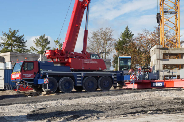 Reims, France - Nov. 2022 - A red, wheeled mobile crane helps to mount a stationary, tower crane, on a construction site on Moulin de la Housse Science Campus of Reims Champagne-Ardenne University
