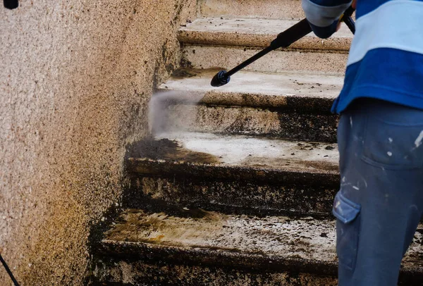 Outdoor work : a maintenance officer cleans and defoams a dirty exterior stone staircase with the lance of a high-pressure washer, while the bad water, charged with moss, trikles down the steps