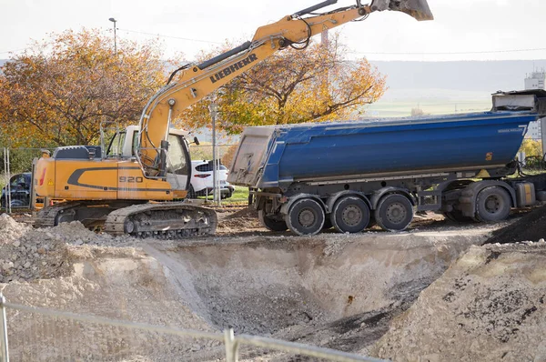 stock image Reims, France - Nov. 2022 - A yellow excavator from the German-Swiss manufacturer Liebherr digs a hole and discharges the earth into a tipper semi trailer, on a construction site on URCA Campus