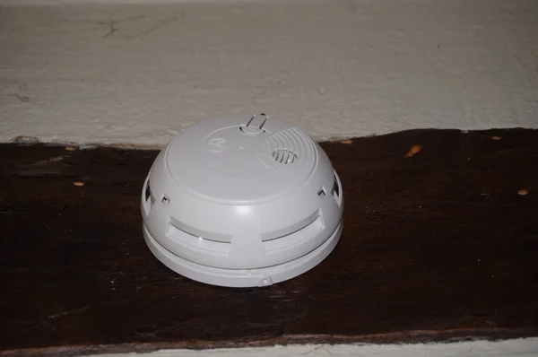 リモート監視システムに接続された木材ビームに固定された丸い煙センサー このような家庭の防火システムは 法的セキュリティ要件に従って フランスで必須です — ストック写真