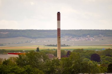 Reims, Fransa - Nisan 2021 - Reims, Reims Dağı ufukta tepelik ve ağaçlık Reims Dağı, Veolia 'nın atık yönetim merkezinde, Remival atık enerji santralinin bacası, uzaktan görüldü
