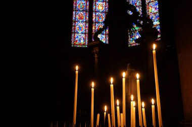 Reims, Fransa - Mart 2021 - Notre-Dame Katedrali 'nin arka planında renkli camlı pencereleri olan, yan şapelin alacakaranlığında parlayan bir dizi dini mum ışığı
