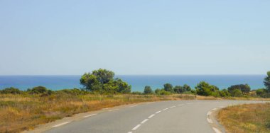 Uzakta, Akdeniz 'in güzel mavi sularının kıyısındaki Narbonne-Plage' ın güneyli tarzı evlerinden geçerek sahil şeridine doğru yol alan yol.
