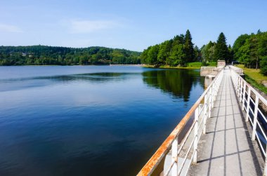 Montagnes Gölü 'nün mavi sularını kaplayan barajın tepesinde bir yaya köprüsü. Güney Fransa' da Mazamet yakınlarında, Montagne Noire tepelerinin ormanlık arazisinde bulunan yapay bir su deposu.