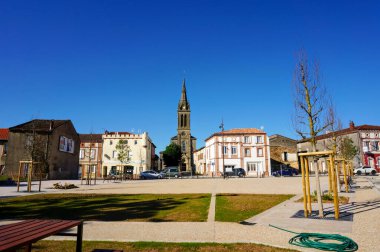 Villefranche d 'Albigeois, Fransa - Mayıs 2020 - Köyün yenilenmiş ana meydanı, genç ağaçlarla döşenmiş, ve Neo-Gotik kilisesinin çan kulesinin domine ettiği eski tuğla evler
