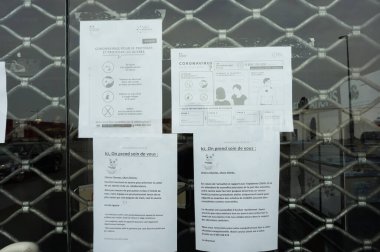 Albi, Fransa - 20 Mart 2020 - Dükkan muhafaza nedeniyle metal kepenkle kapatıldı; resmi talimatlar ve Covid-19 salgınıyla ilgili posterler cam penkte sergileniyor