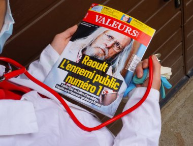 Marseille, France - May 2020 - A medical doctor in white blouse points the finger at a journal featuring Pr Didier Raoult, the world-famous researcher advocating the 
