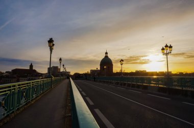 Fransa 'nın Toulouse kentindeki Pont Saint-Pierre köprüsünün korkuluk ve sokak lambalarıyla birlikte Saint-Joseph de La Grave Kilisesi' nin kubbesine doğru gün batımı görüntüsü ve perspektif efekti