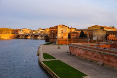 Port Viguerie 'nin Toulouse, Fransa' daki Garonne Nehri kıyısındaki gün batımı manzarası; Saint-Jacques ve Saint-Cyprien ilçelerindeki kemerli Pont-Neuf köprüsü ve tuğla konak evleri