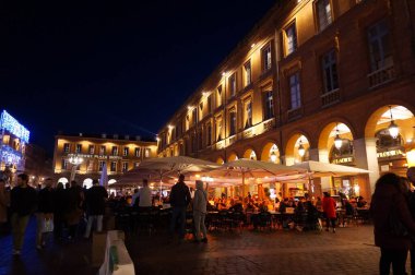 Toulouse, Fransa - 2019 - Pembe Şehir 'de gece hayatı, insanların kalabalık Capitole Meydanı' nın kemerli atari salonlarının dibinde, restoran teraslarının şemsiyeleri altında iyi vakit geçirmeleri.