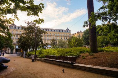 Toulouse, Fransa - Temmuz 2020 - Charles de Gaulle Meydanı 'nın yapraklı bahçesinde ahşap banklar, ağaçlar ve kum tabanı, Capitole' nin arkasında, arka planda zarif bir Haussmann kasaba binası